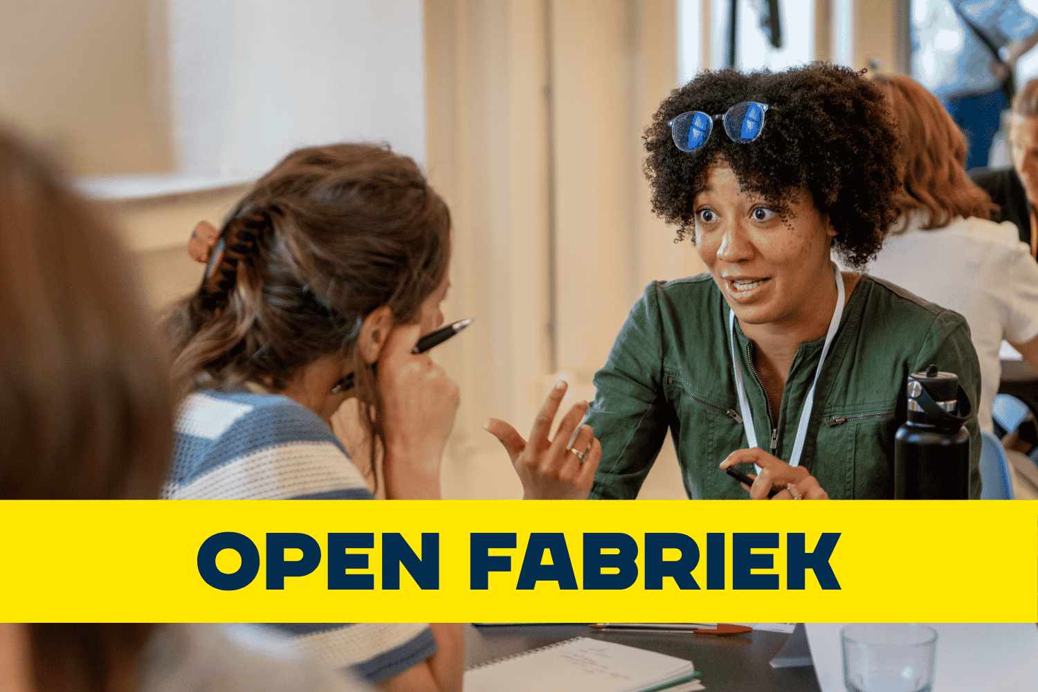 Foto van twee personen die praten aan een tafel met de tekst "open fabriek".
