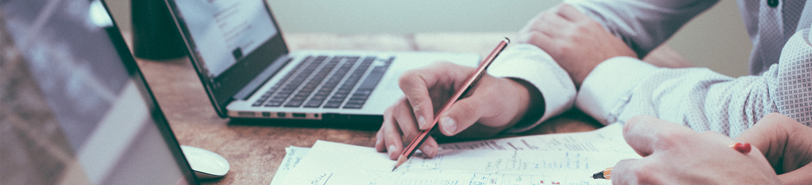 Hand schrijft op blad naast laptops